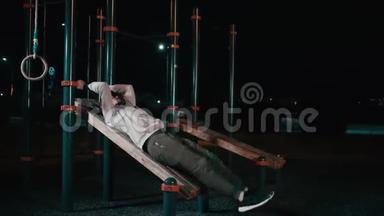年轻的运动员正在夜间公园里用运动器材抬腿
